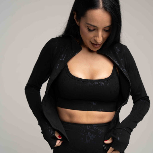 Woman wearing a black sports bra and jacket against a gray background