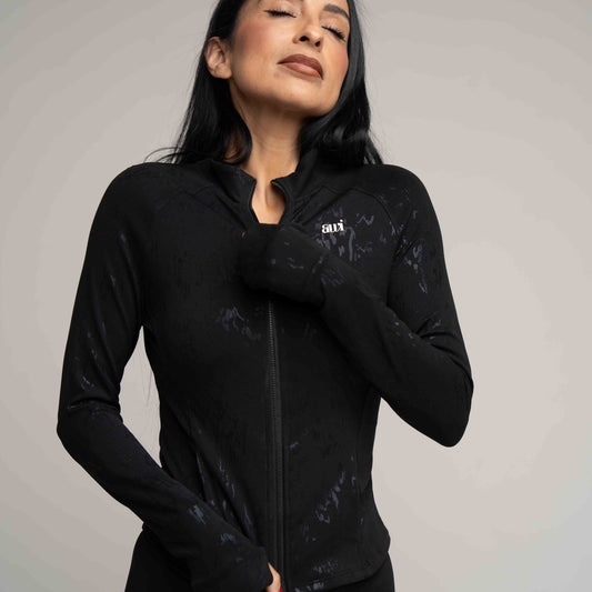 Woman wearing a black jacket with a logo on a gray background