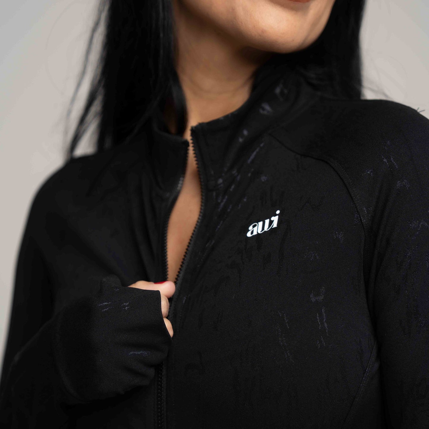 Person wearing a black jacket with 'avi' logo on a neutral background