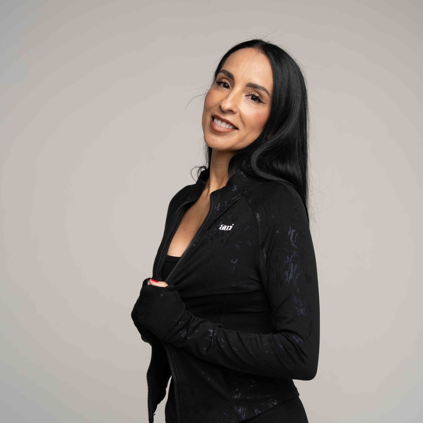 Woman wearing a black jacket with a logo on a gray background