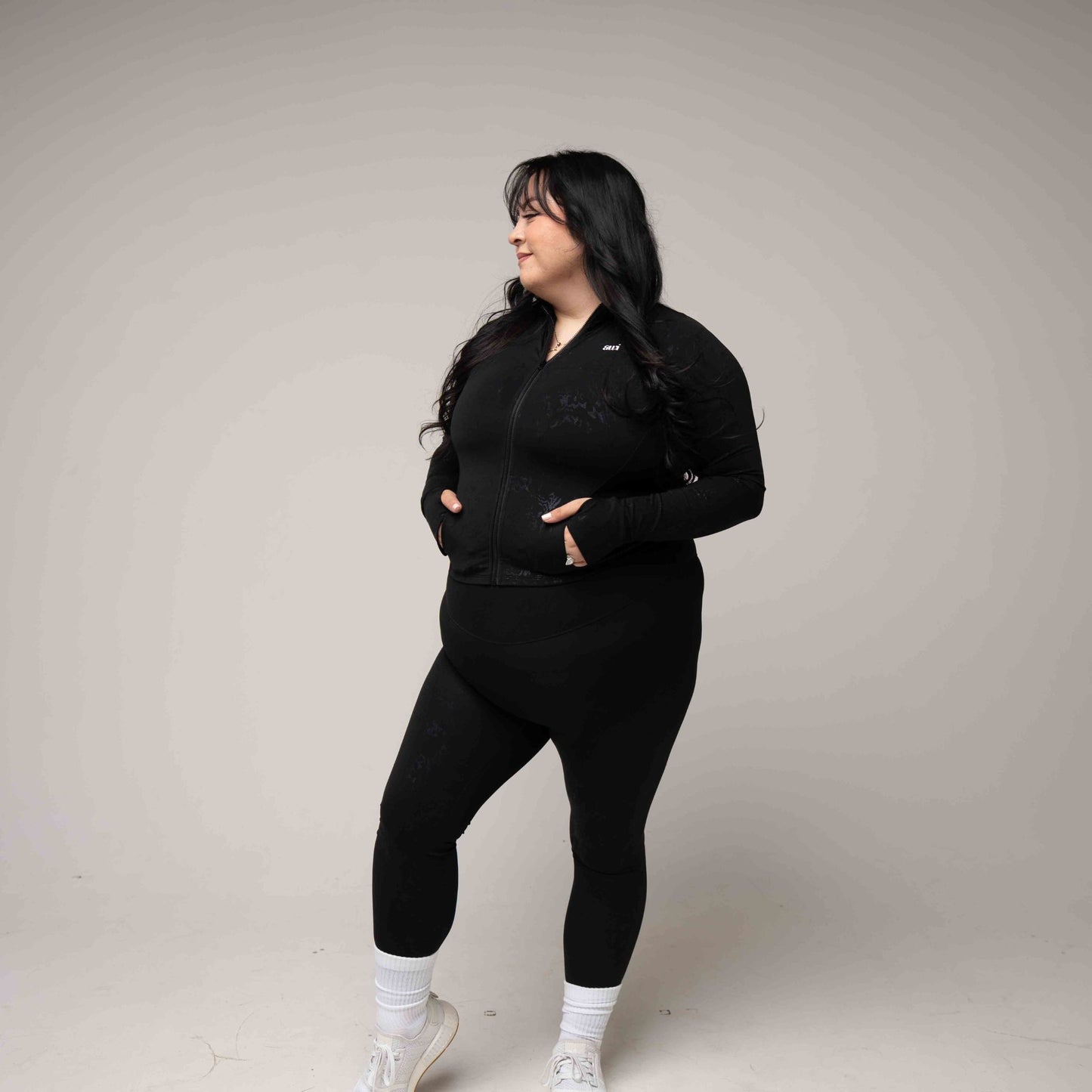 Person wearing a black outfit with white sneakers on a plain background