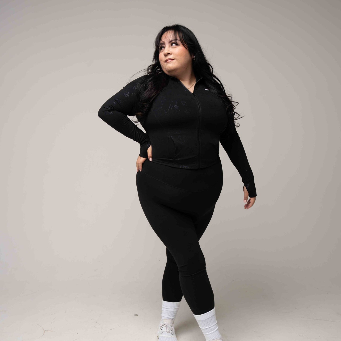 Woman wearing a black outfit with white sneakers on a plain background