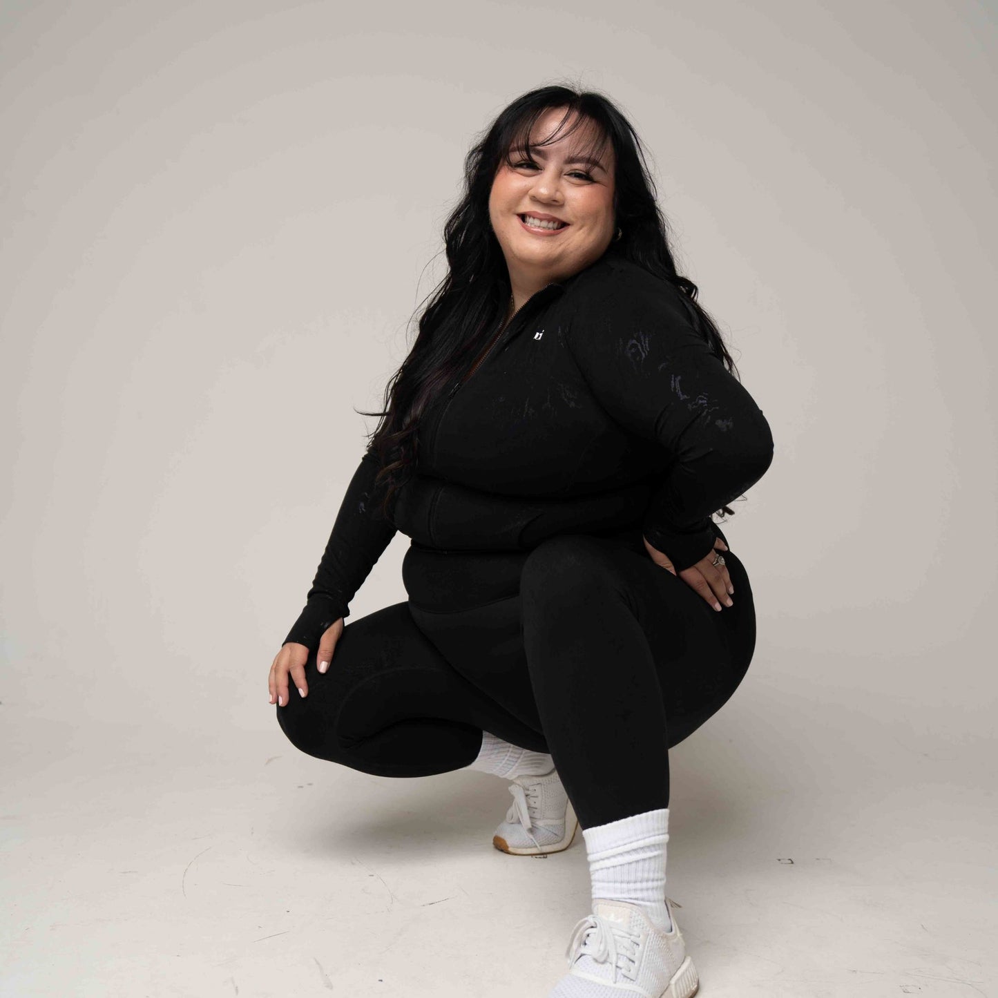 Person wearing a black outfit with white sneakers on a plain background
