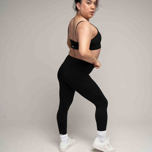 Person wearing black sports bra and leggings on a plain background