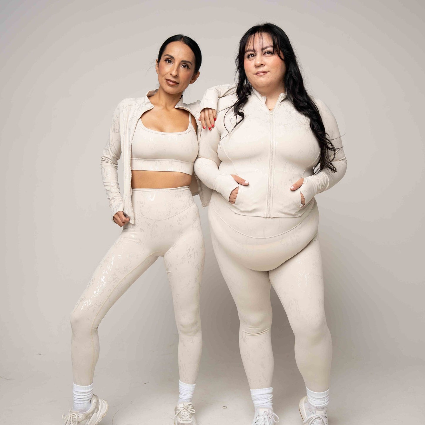 Two women wearing matching light beige outfits against a plain background