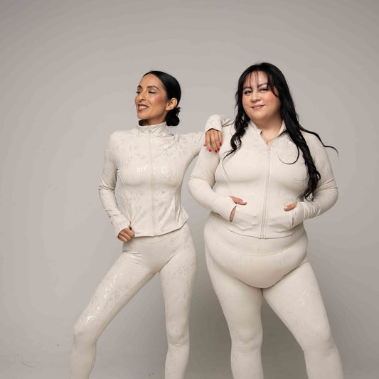 Two women wearing matching light beige outfits against a plain background