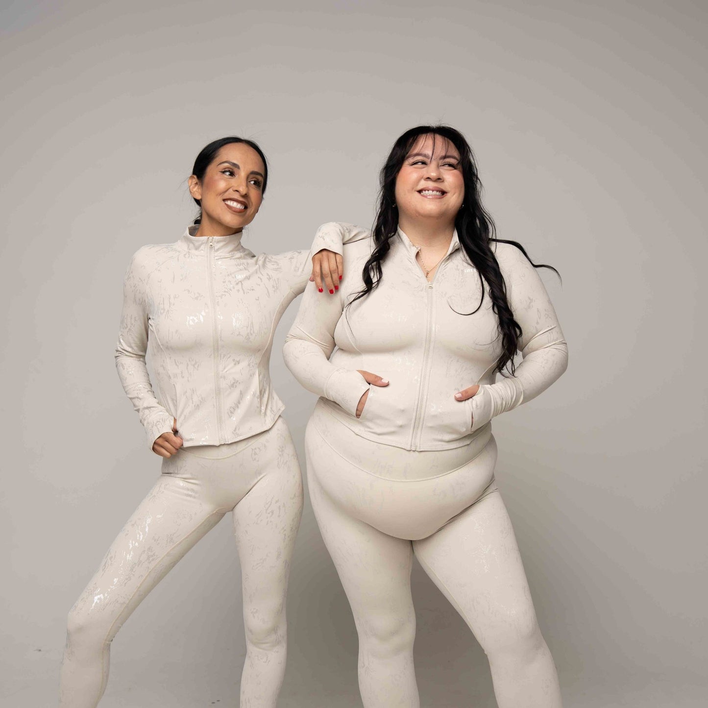 Two women wearing matching lihht beige outfits against a plain background