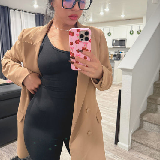 Person wearing a beige coat and black unitard, holding a phone with a cherry design, in a home setting.