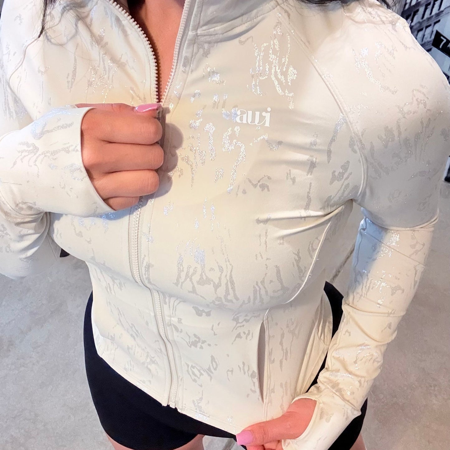 Front view of cream fitted zip-up jacket with metallic-textured detail and thumbholes, paired with high-waisted black scrunch shorts from the Avvi oat mood collection.