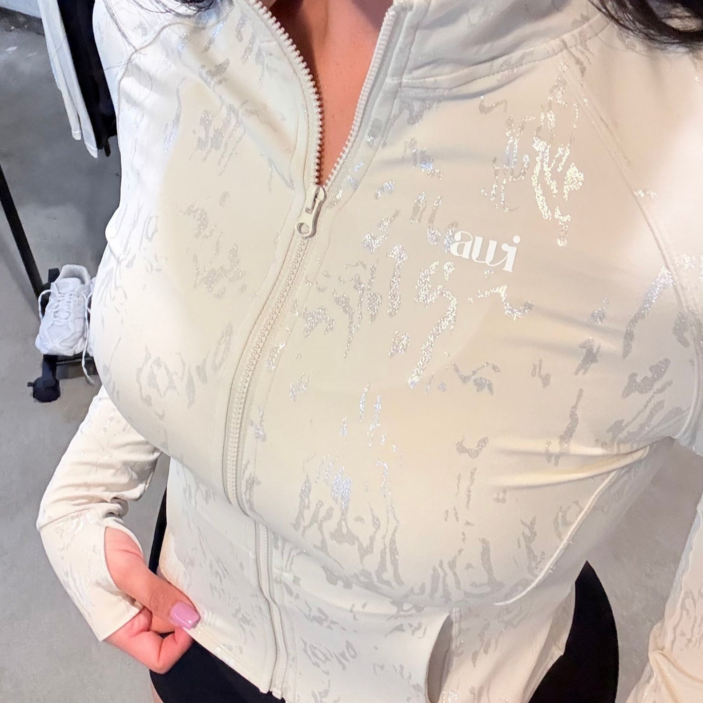 Front view of cream fitted zip-up jacket with metallic-textured detail and thumbholes, paired with high-waisted black scrunch shorts from the Avvi oat mood collection.