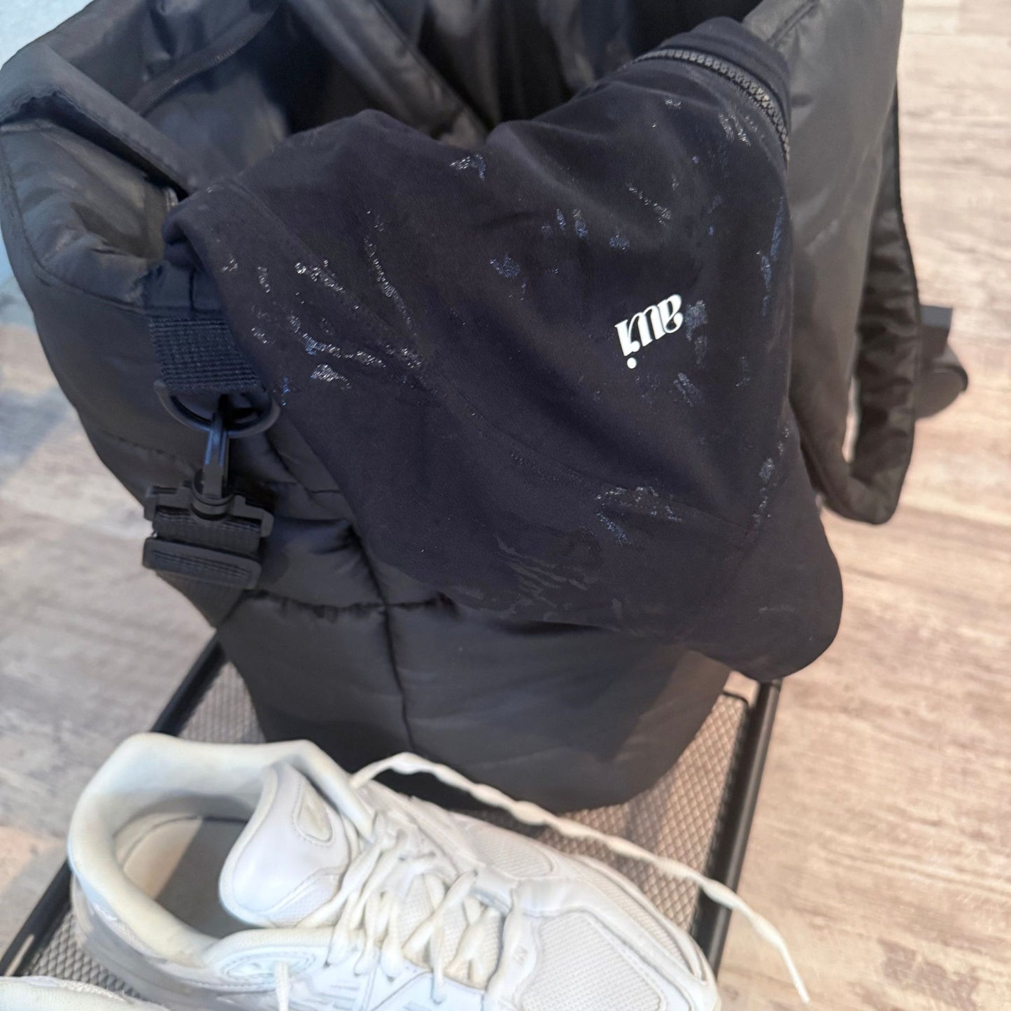 Black Avvi jacquard jacket draped over a puffer gym bag, next to white athletic sneakers on a mesh shelf.