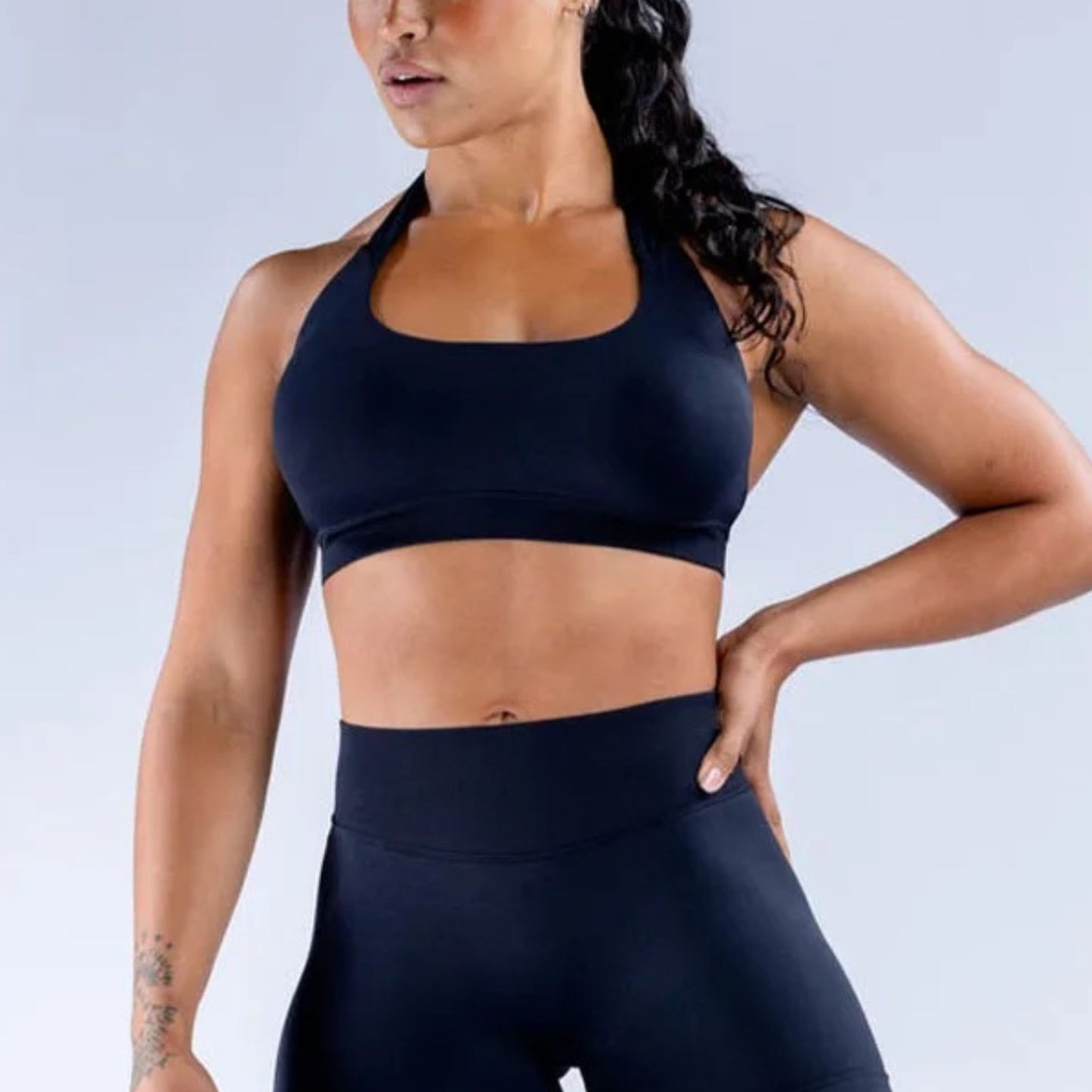 Woman wearing a black sports bra and leggings on a light gray background