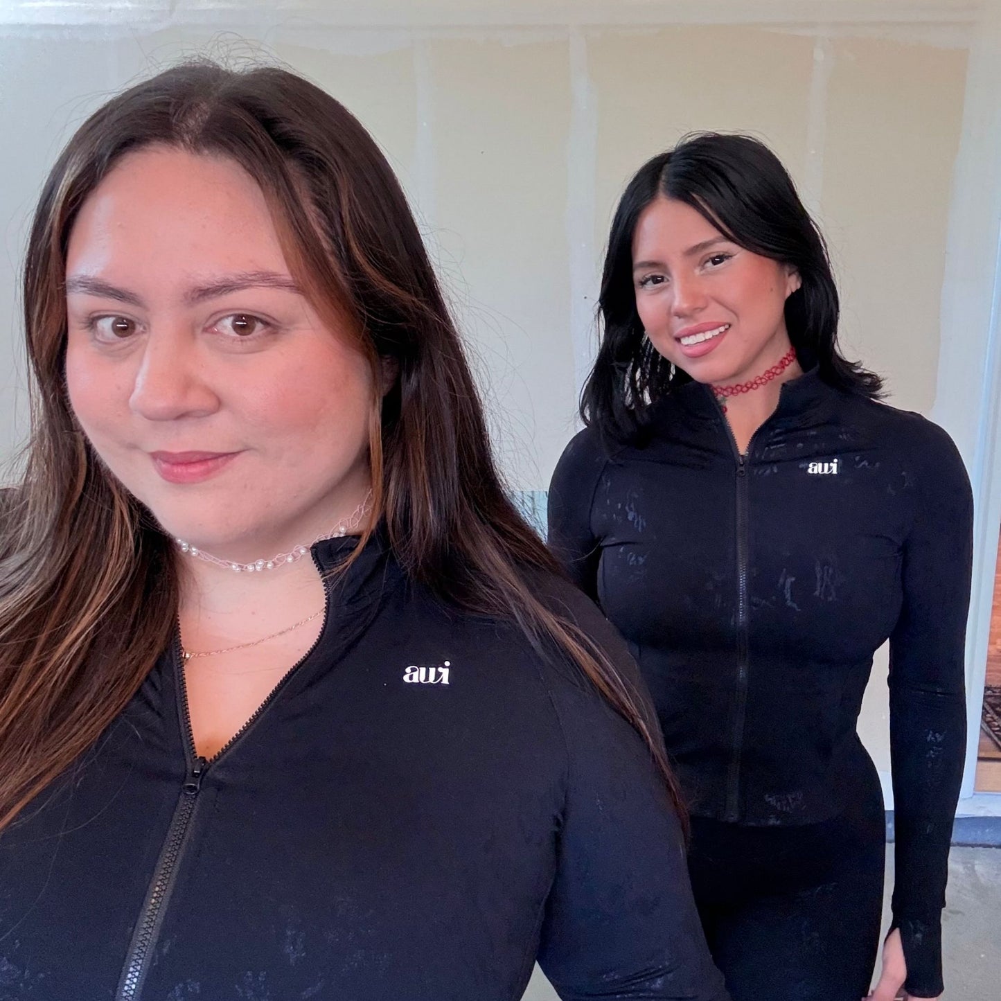 Two women side by side wearing matching Avvi black jacquard zip jackets, showing diverse body types and styling.