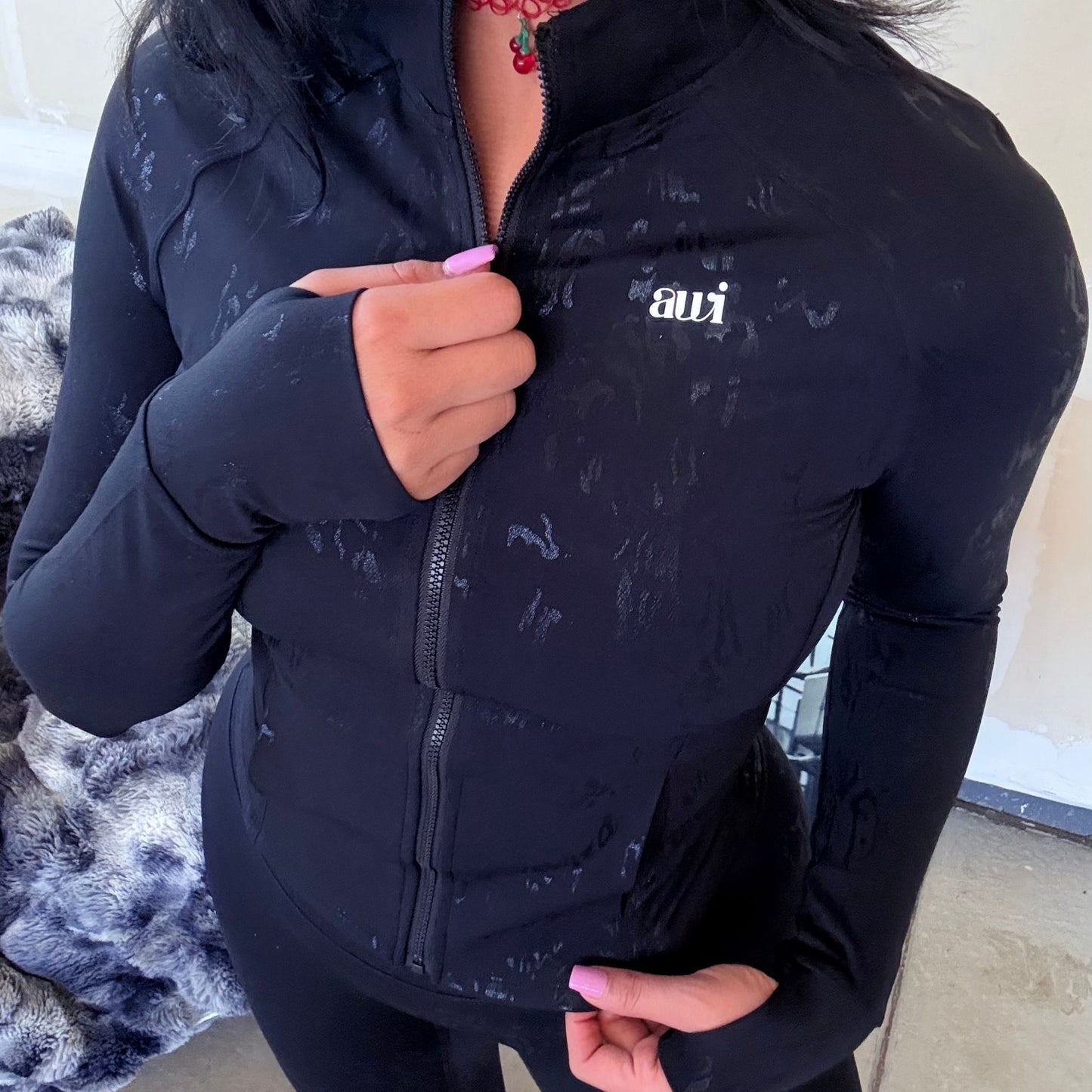 Woman styling the Avvi black jacquard zip-up jacket, showing close-up of chest and logo.