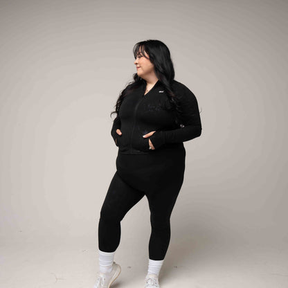 Person wearing a black outfit with white sneakers on a plain background