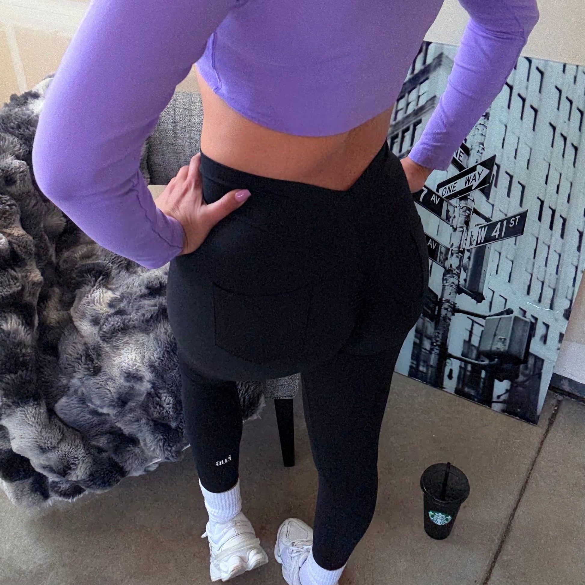 Back view of the Lilac long sleeve Studio Layer Crop Top, worn with black V-Neck Scrunch Leggings and white sneakers in a studio setting.