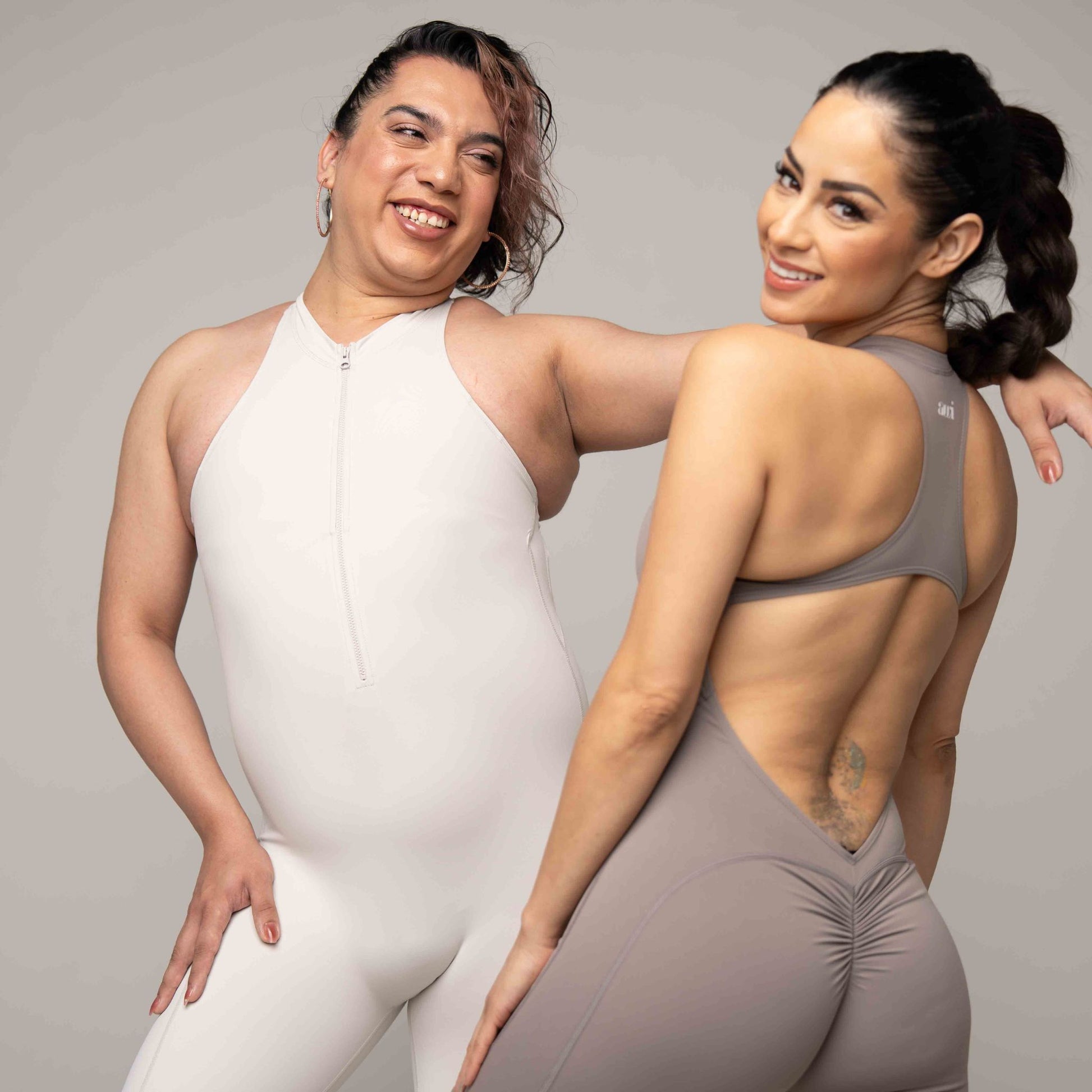 Two women posing together, one in a white outfit and the other in a gray outfit.