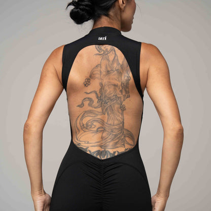 Person wearing a black sleeveless top with a detailed tattoo on the back against a neutral background