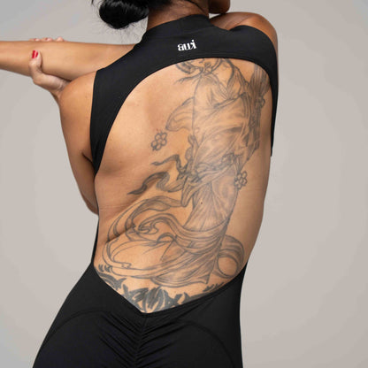 Person wearing a black sleeveless top with a large tattoo on the back against a neutral background