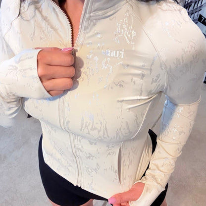 Front view of cream fitted zip-up jacket with metallic-textured detail and thumbholes, paired with high-waisted black scrunch shorts from the Avvi  oat mood collection.