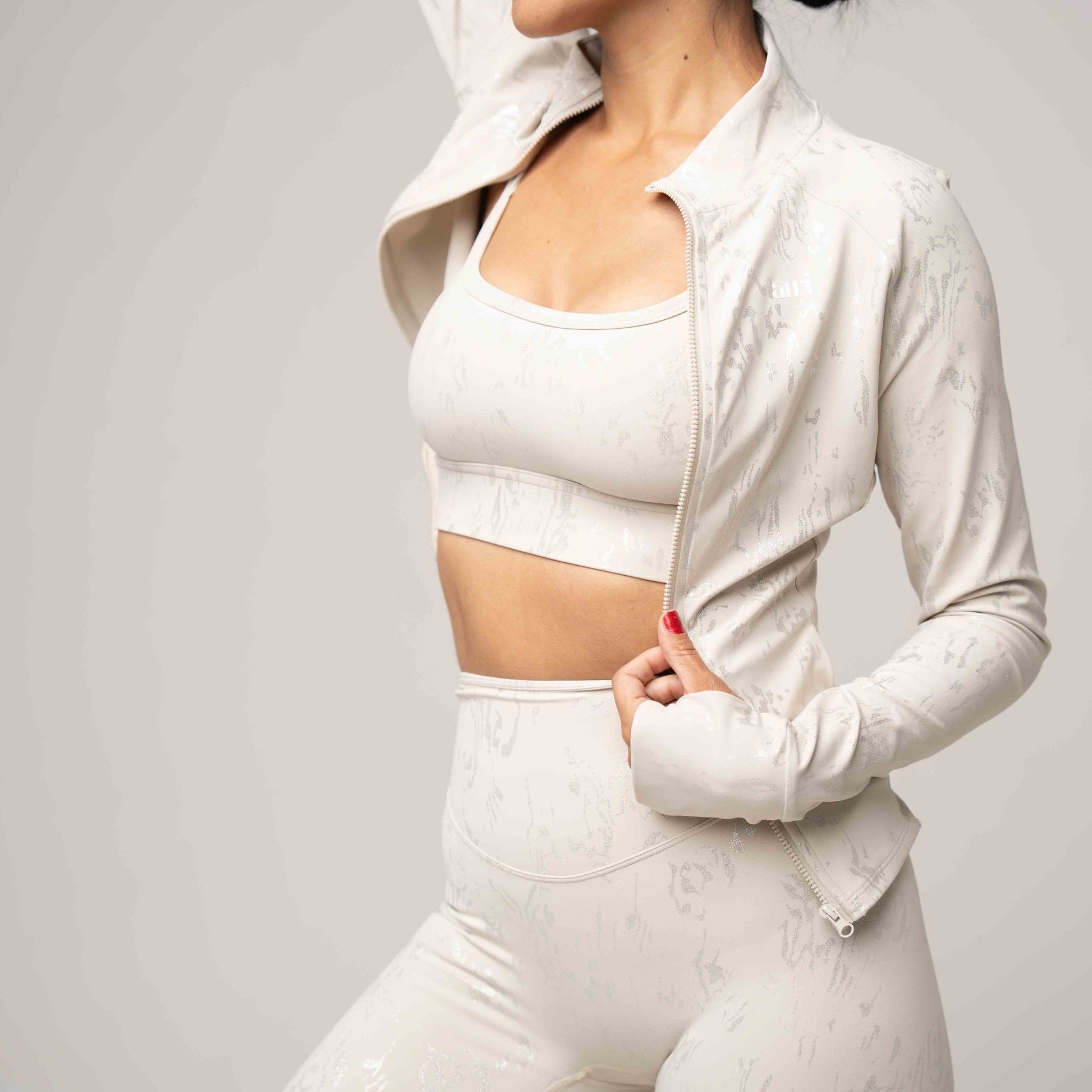 Woman wearing a light beige athletic outfit with a jacket on a plain background