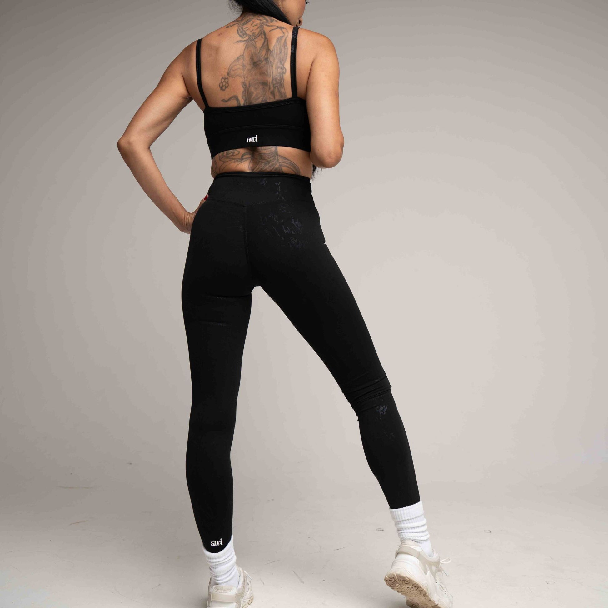 Person wearing black athletic leggings and sports bra on a plain background