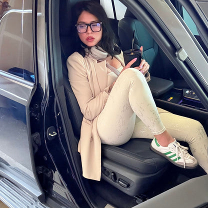 Woman wearing a neutral blazer over a soft oat matching set, sitting in a car with a drink in hand — styled for a comfy airport outfit