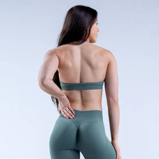 Woman wearing a green sports bra and leggings on a light gray background